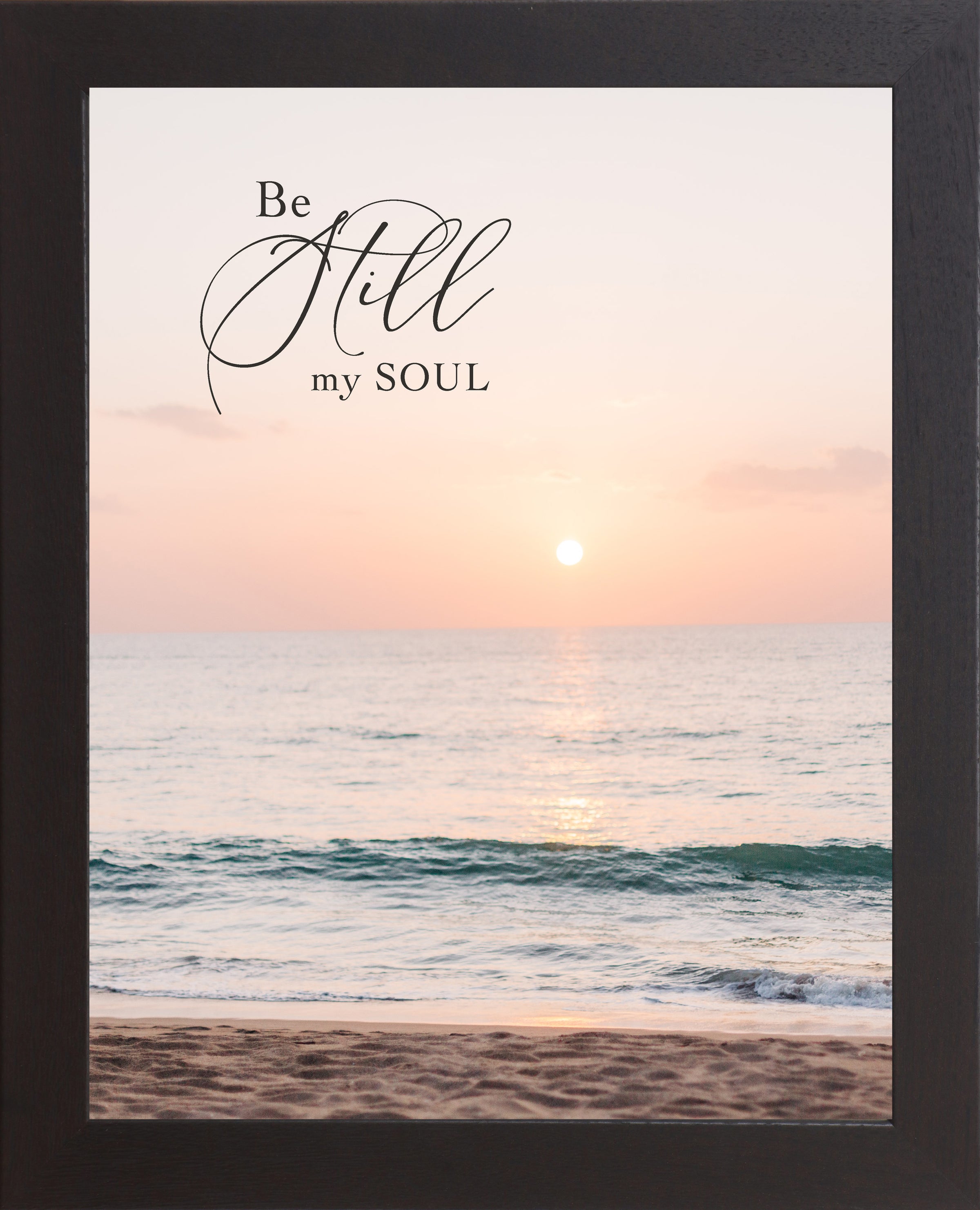Black framed portrait Christian wall art with the words Be Still My Soul in elegant script set against a soft peach and coral beach sunset with teal ocean waves and sandy shoreline