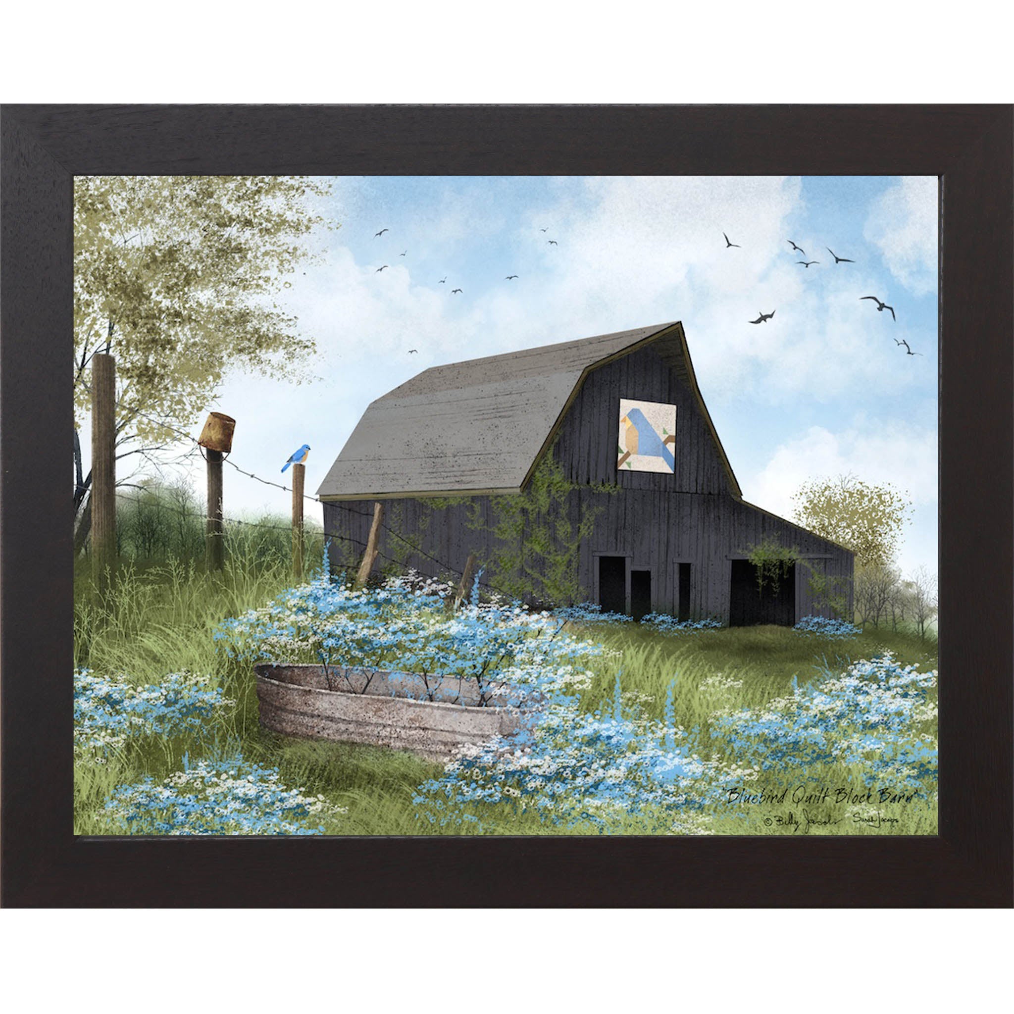 Black framed Billy Jacobs Bluebird Quilt Block Barn wall art featuring a weathered gray gambrel barn with a bluebird quilt block on its face surrounded by blue and white wildflowers a metal stock tank a bluebird on a fence post and spring trees