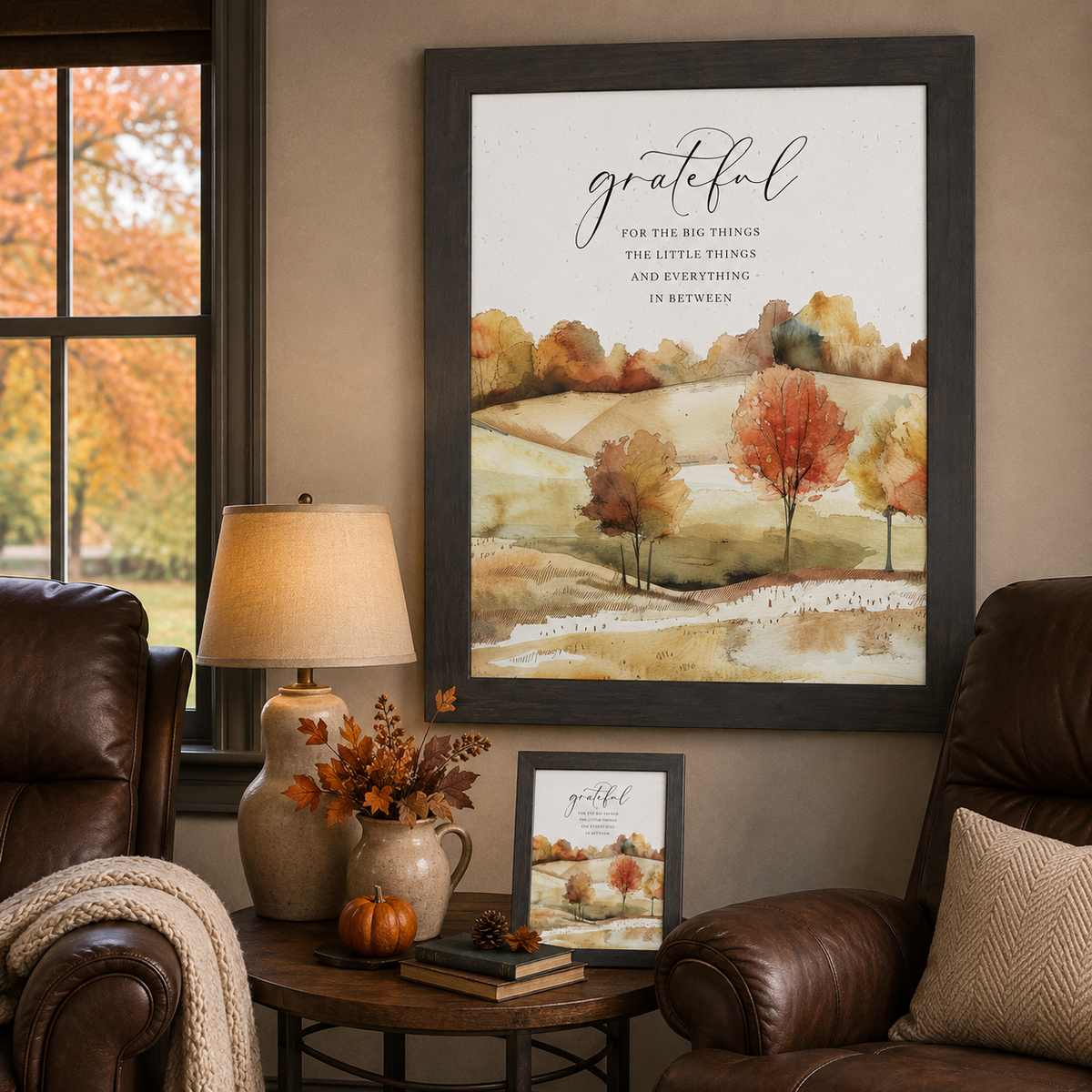 Slatewood dark framed Grateful for the Big Things autumn hills wall art NS361 displayed large in cozy fall den beside leather armchairs with fall view through window — ceramic jug lamp fall branches pumpkin pine cone and easel back on side table — watercolor rolling autumn hills with vivid red orange and gold trees and grateful script typography