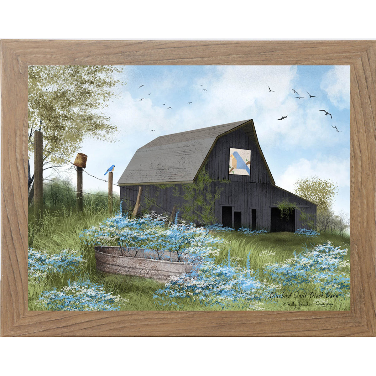 Farmtable framed Billy Jacobs Bluebird Quilt Block Barn wall art featuring a weathered gray gambrel barn with a bluebird quilt block on its face surrounded by blue and white wildflowers a metal stock tank a bluebird on a fence post and spring trees