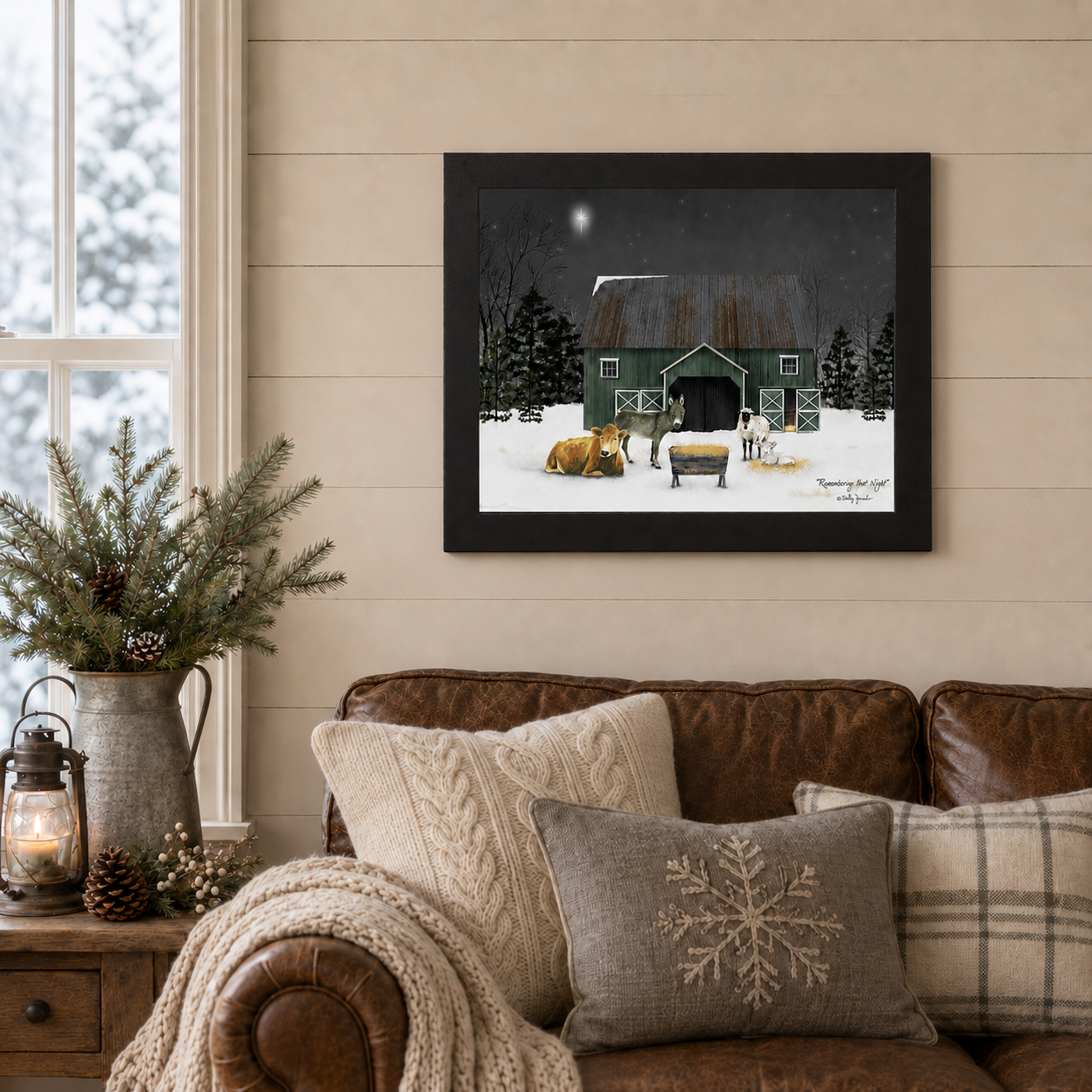 Black framed Billy Jacobs "Remembering That Night" landscape print displayed above a leather sofa in a cozy farmhouse living room with shiplap walls, pine branches in a galvanized pitcher, a lit lantern, and snowflake accent pillows