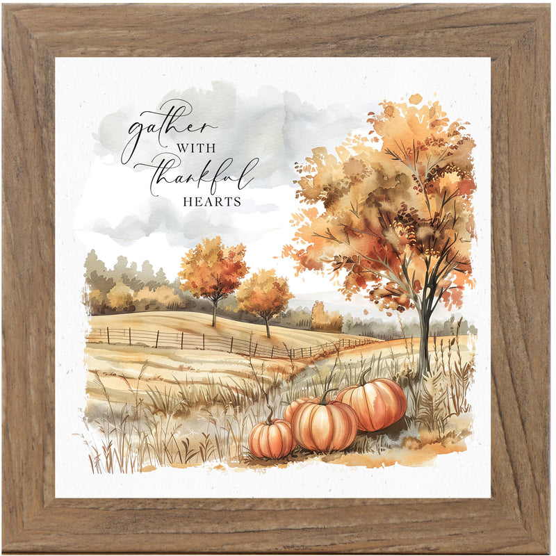 Framed fall art with pumpkins in a brown farm field, turning trees, and the quote “Gather With Thankful Hearts” in warm watercolor tones